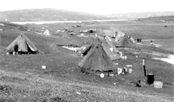 Black and white photograph of a military encampment with multiple canvas tents scattered across open, grassy terrain, likely RAF Sumburgh during wartime, with hills and water visible in the background